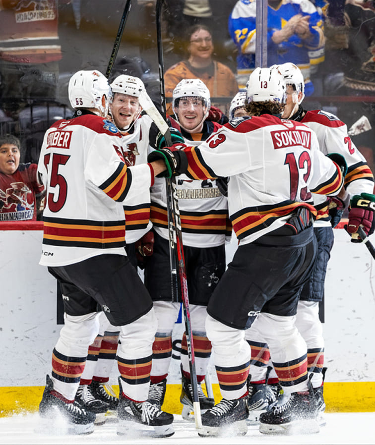 a group of ice hockey players in white jerseys smiling and celebrating a goal together on the ice